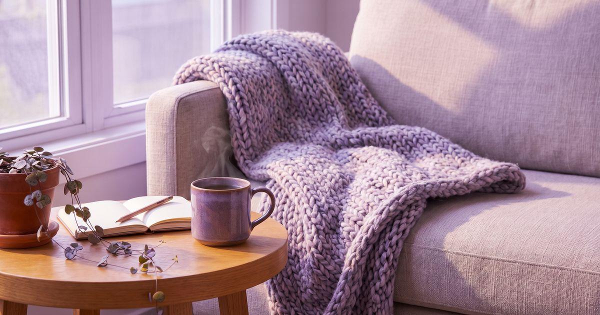 A sofa corner with a knitted throw, an open notebook and pencil, a mug of herbal tea and a trailing houseplant in soft light.