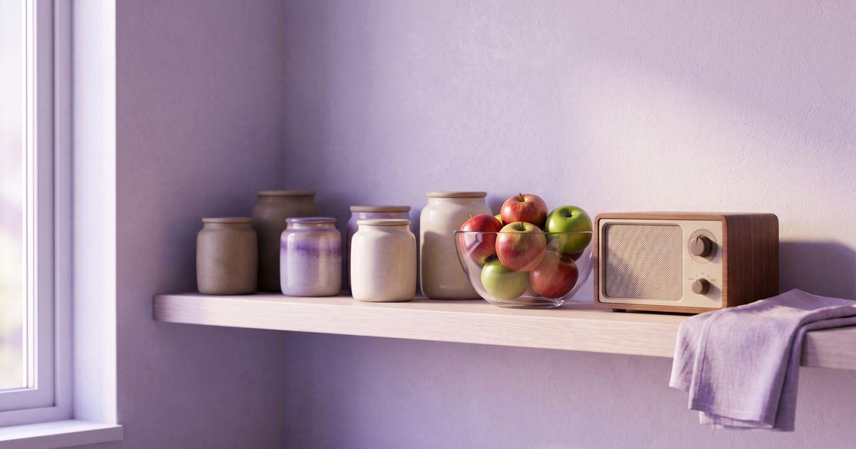A kitchen shelf with closed ceramic jars, a glass bowl of apples and a small radio turned down, in calm daylight.