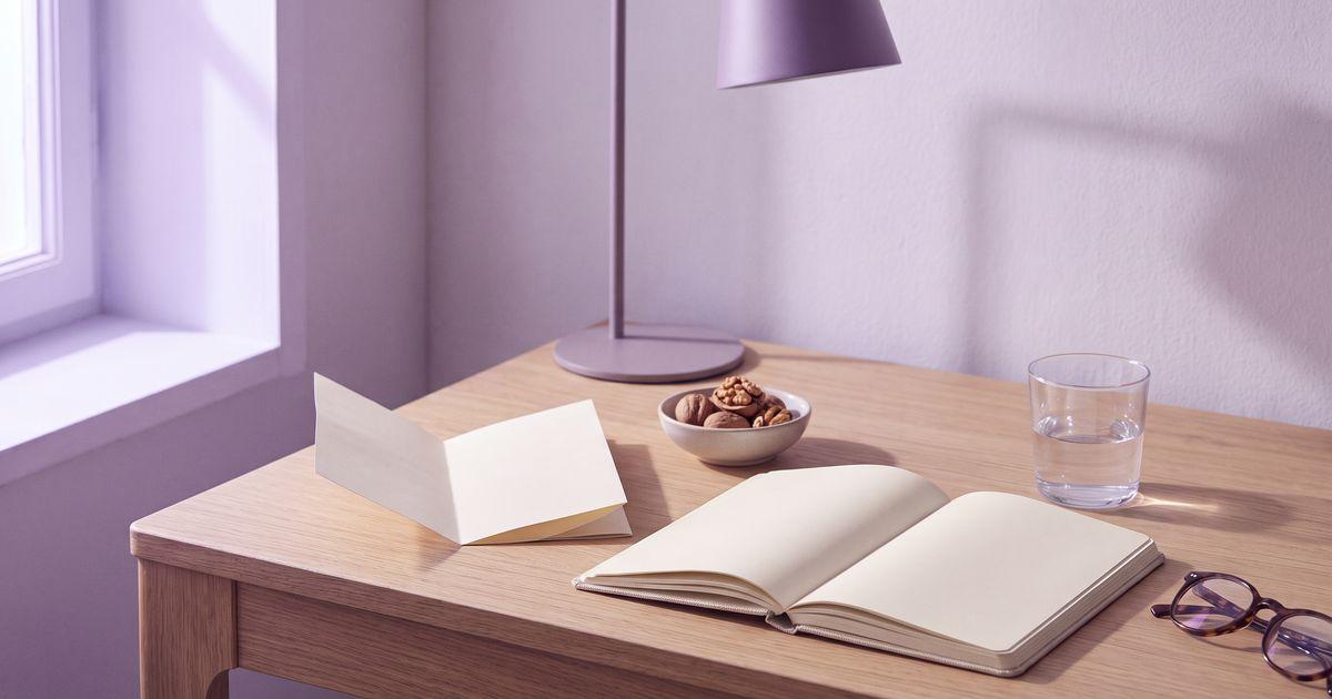 An open notebook with handwritten notes, a glass of water, a paper leaflet, walnuts and reading glasses on an oak desk.